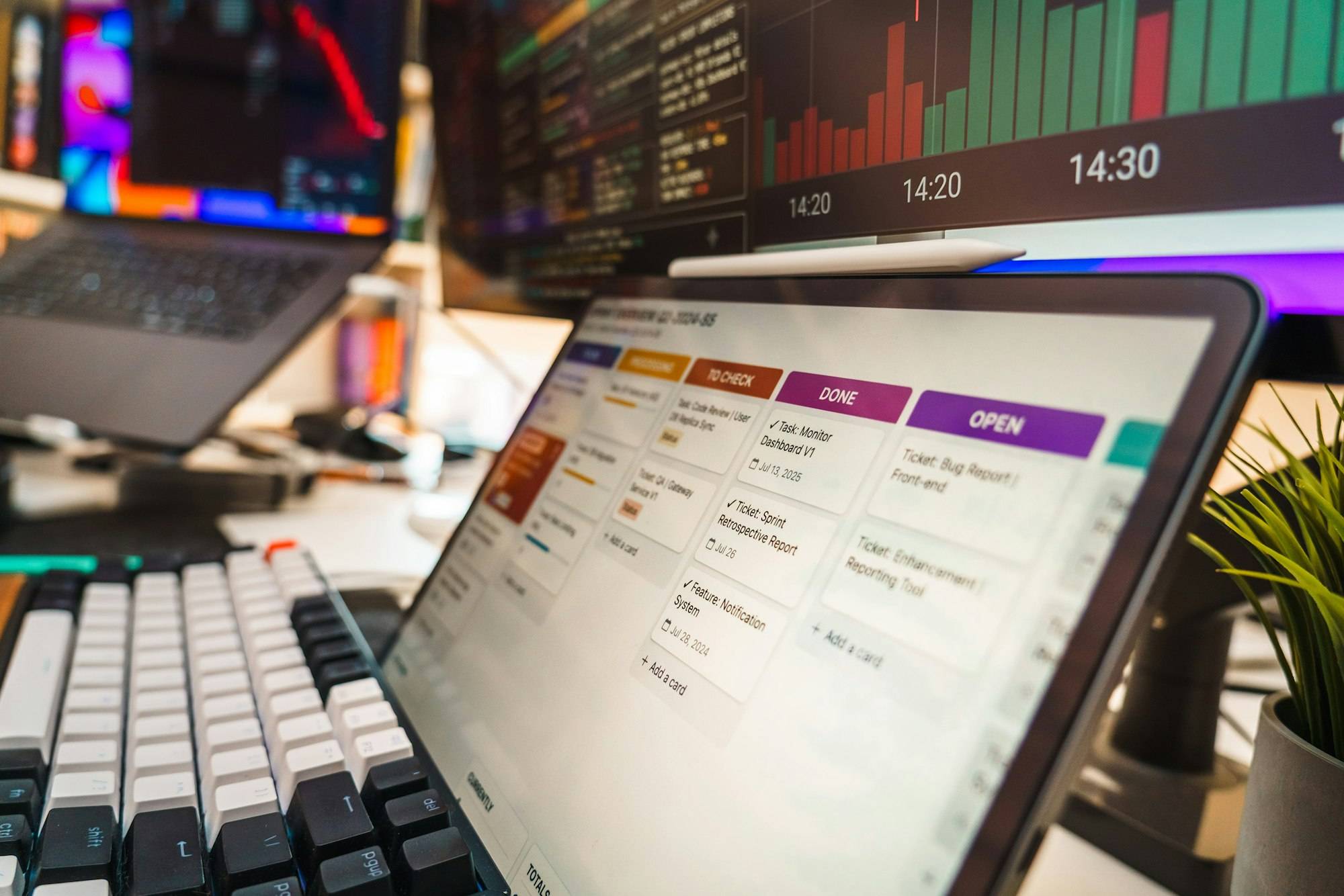 Tablet mit einer Aufgabentafel auf dem Schreibtisch, im Hintergrund ein Monitor mit Balkendiagramm